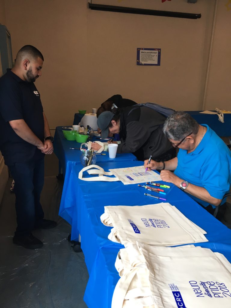 DCRC staff member Jose G. watches as event attendees paint their neurodiversityy pride bags.
